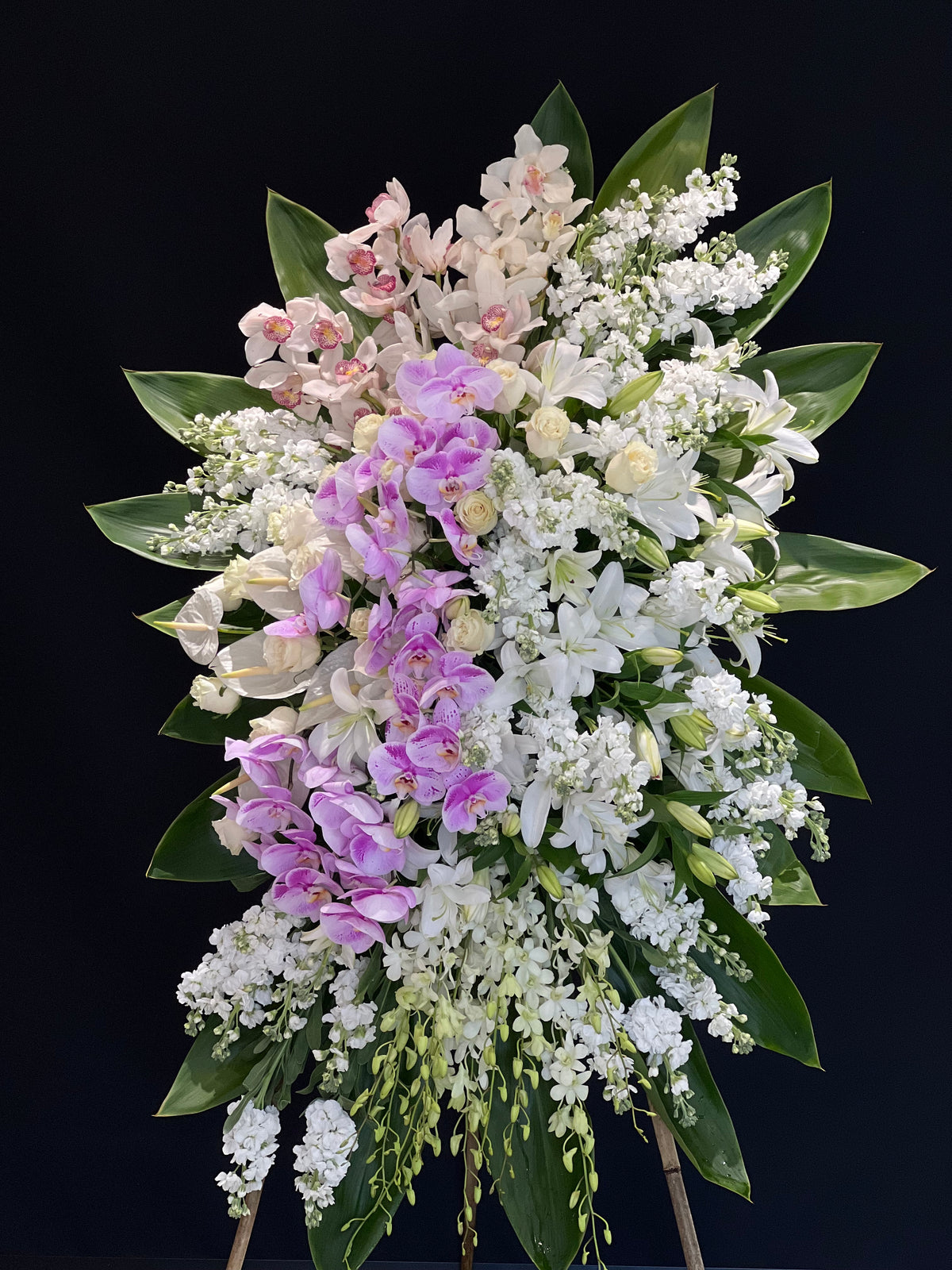A tender standing floral spray in soft pink and white, featuring stocks, roses, cymbidium orchids, dendrobium orchids, lilies, and the exquisite addition of purple phalaenopsis orchids. A compassionate floral tribute from Yonge Florist, offering comfort and sympathy for funerals and memorial services. Available for local GTA delivery to funeral homes, churches, chapels, and mosques.