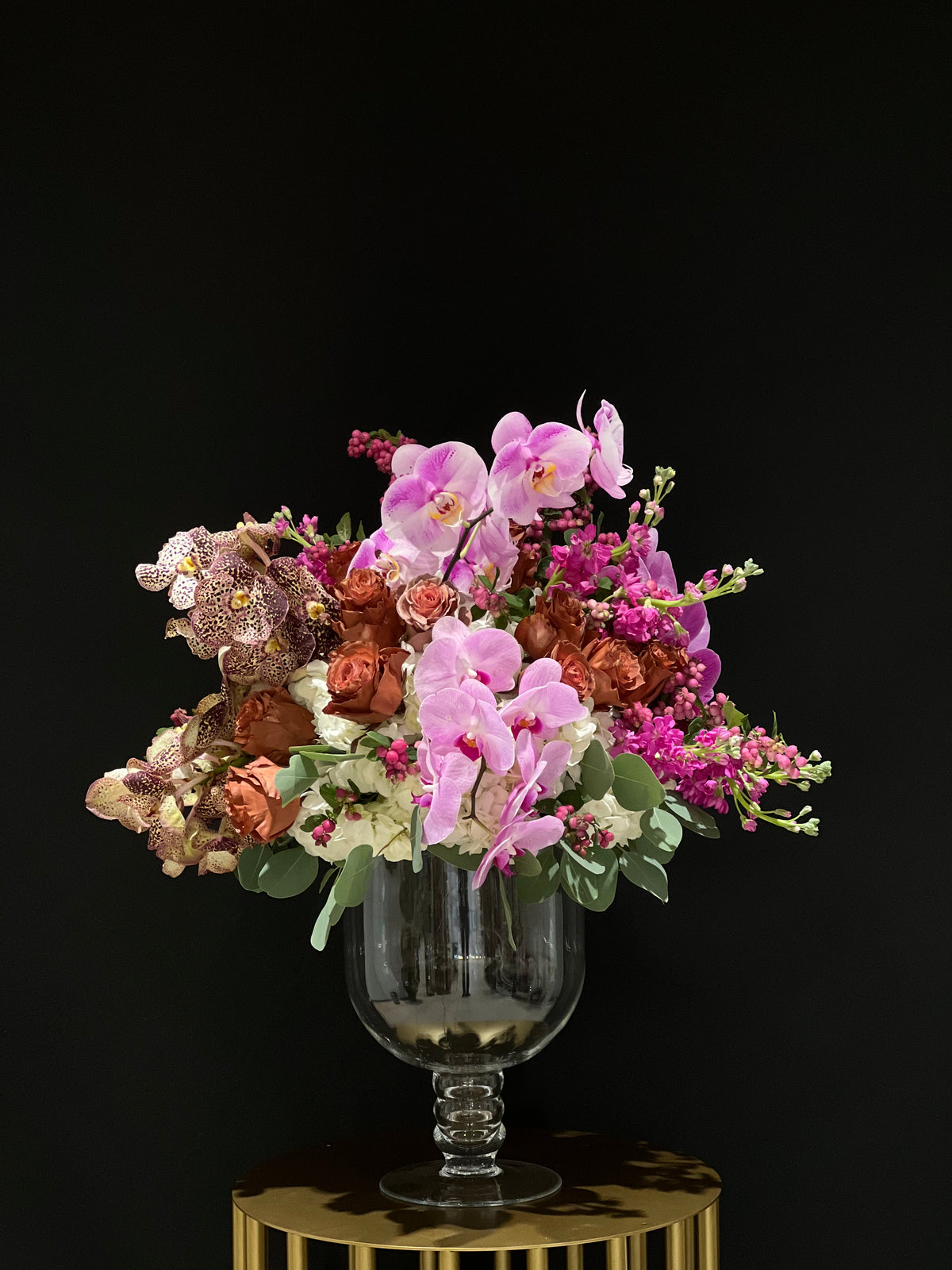Alt tag: A breathtaking vase arrangement featuring Vanda and Phalaenopsis orchids, roses, stocks, and hydrangea in an elegant clear urn-style vase. Perfect for various occasions, meticulously curated with a stunning display in mind. Yonge Florist's exquisite creation.