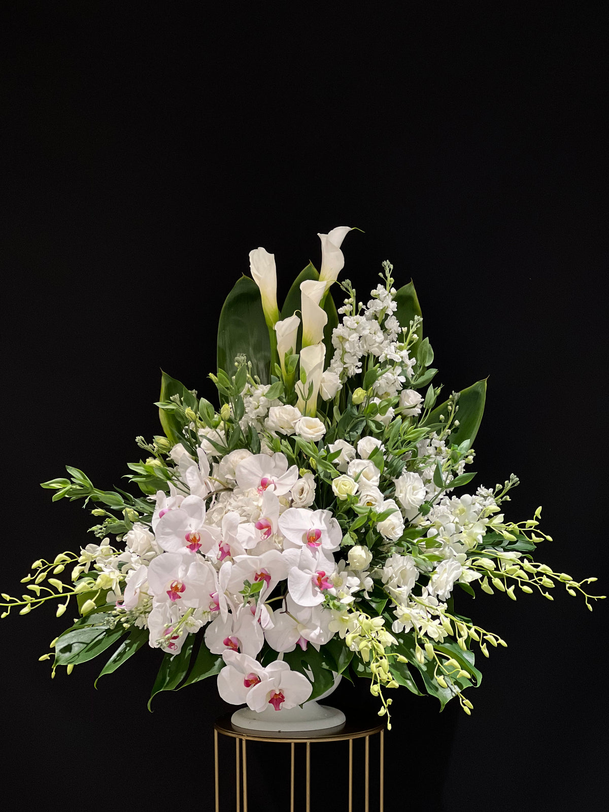 Angelic White Funeral Basket Arrangement: A serene and elegant tribute with white Calla Lilies, Stocks, Roses, Lisianthus, and Dendrobium Orchids, beautifully accented with Phalaenopsis Orchids.