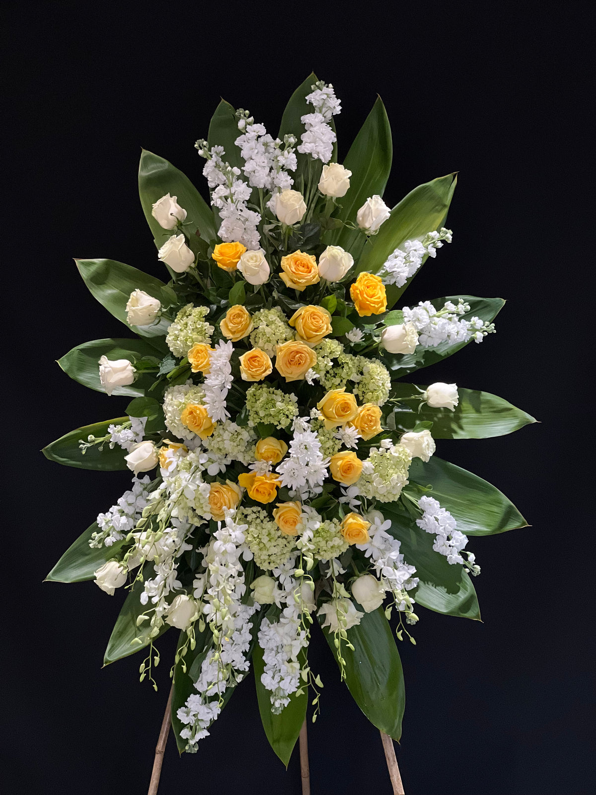 A serene standing floral spray in yellow and white, featuring stocks, roses, dendrobium orchids, hydrangeas, and daisies. An elegant floral tribute from Yonge Florist, offering comfort and sympathy for funeral and memorial services. Local GTA delivery to funeral homes, churches, chapels, and mosques available