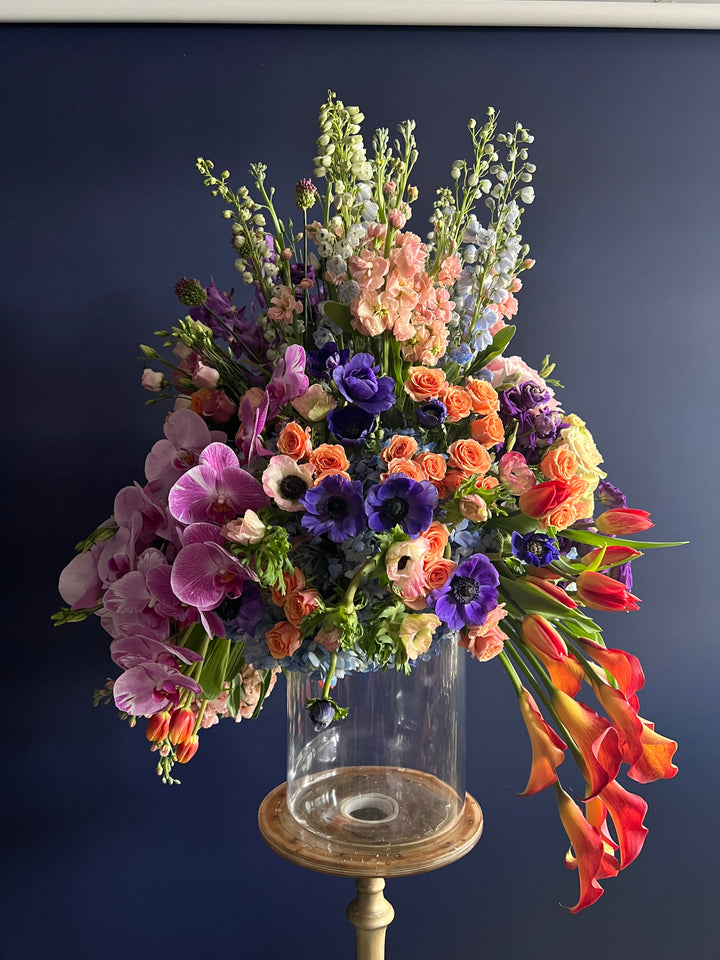 "Vivid Harmony Floral Arrangement: A burst of nature's colors featuring delphiniums, stocks, anemones, lisianthus, tulips, orchids, and mini calla lilies. Perfect for congratulating a new home, celebrating anniversaries, or sending birthday wishes. Expertly crafted by Yonge Florist for local and GTA flower delivery." front photo dark